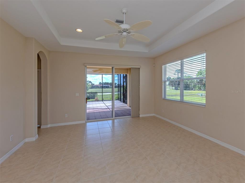 An empty room with tile flooring, a tray ceiling with a fan, and sliding glass doors — 101 MESTRE PLACE, NORTH VENICE, FL