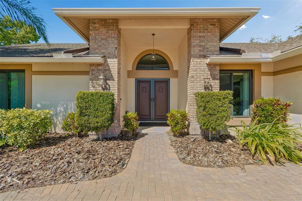 A brick-accented entryway features double doors, a semi-circular window, and a paved walkway — 8723 ASHBURY DRIVE, HUDSON, FL