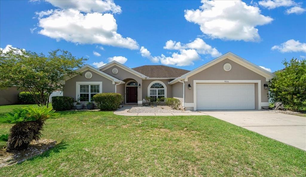 A single-story house with a beige stucco exterior, a two-car garage, and a front lawn — 9870 SW 55TH AVENUE ROAD, OCALA, FL