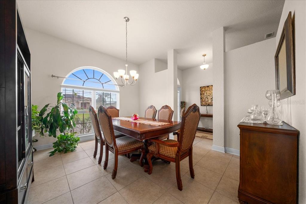 A dining room with a wooden table, six chairs, tile flooring, and an arched window — 9870 SW 55TH AVENUE ROAD, OCALA, FL