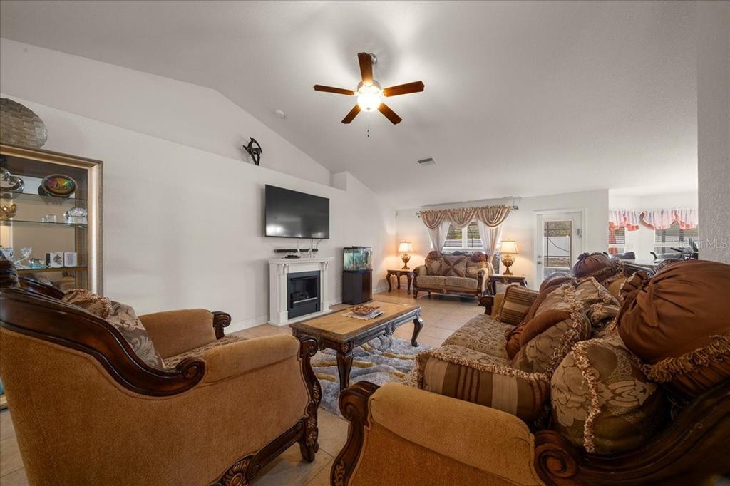 A living room features a vaulted ceiling, a fireplace, and traditional patterned furniture — 9870 SW 55TH AVENUE ROAD, OCALA, FL