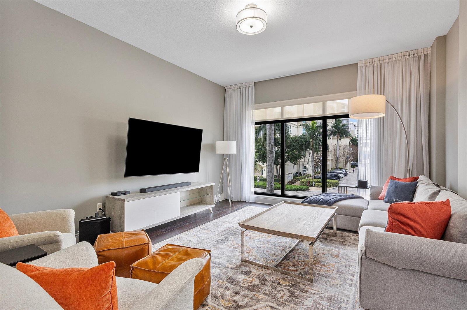 A modern living room features a wall-mounted television, a sectional sofa, and floor-to-ceiling windows — 200 E Palmetto Park Road # 10, Boca Raton FL 33432, BOCA RATON, FL