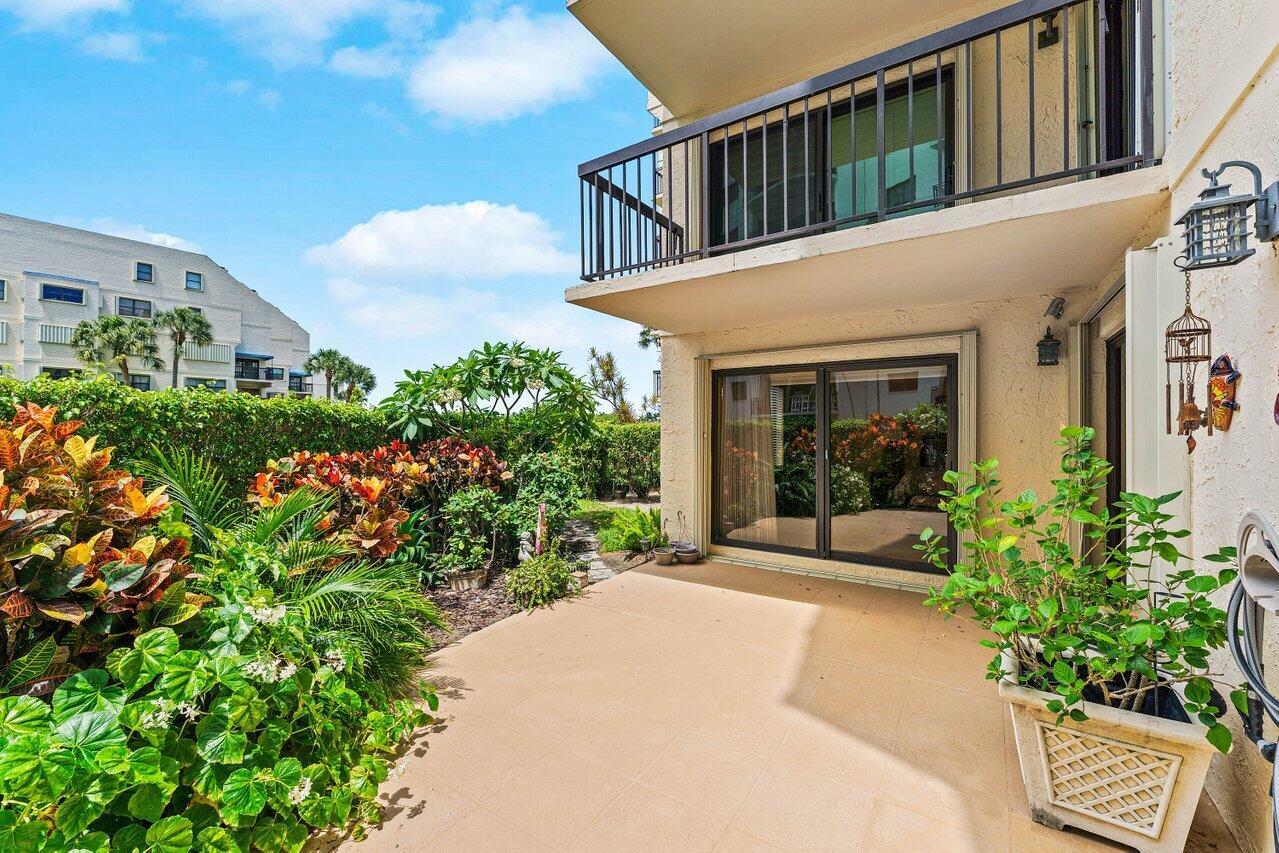 A ground-level patio with a sliding glass door, a balcony above, and surrounding tropical landscaping — 372 Golfview Road # 101, North Palm Beach FL 33408, NORTH PALM BEACH, FL