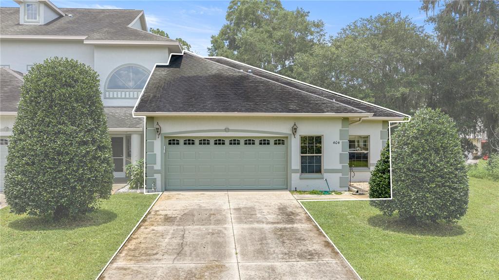 A single-story house exterior features a green garage door, a concrete driveway, and landscaping — 3415 W ANTHONY ROAD UNIT 404, OCALA, FL
