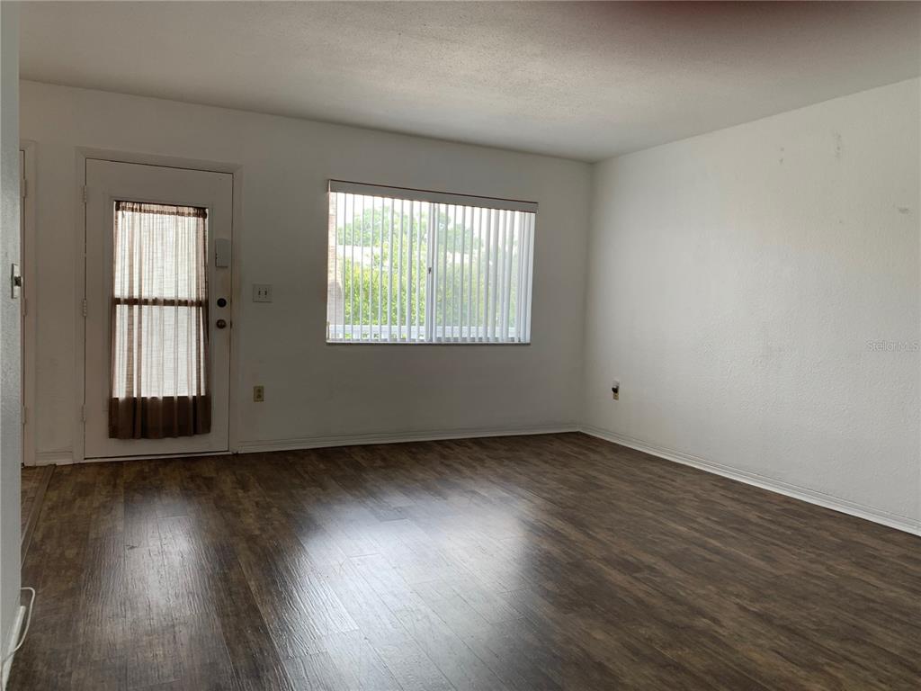 An empty room features wood-look flooring, a white door with a window, and vertical blinds — 8126 112TH STREET UNIT 203, SEMINOLE, FL