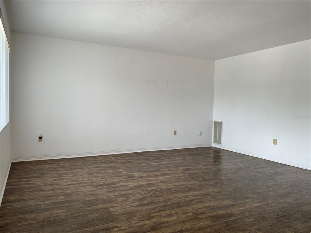 An empty room features white walls, dark wood-look flooring, and a wall-mounted air vent — 8126 112TH STREET UNIT 203, SEMINOLE, FL