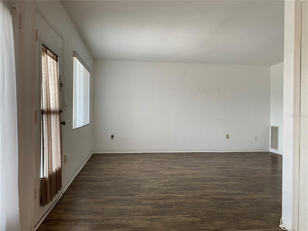 An empty room with wood-look flooring, white walls, a glass door, and vertical blinds — 8126 112TH STREET UNIT 203, SEMINOLE, FL