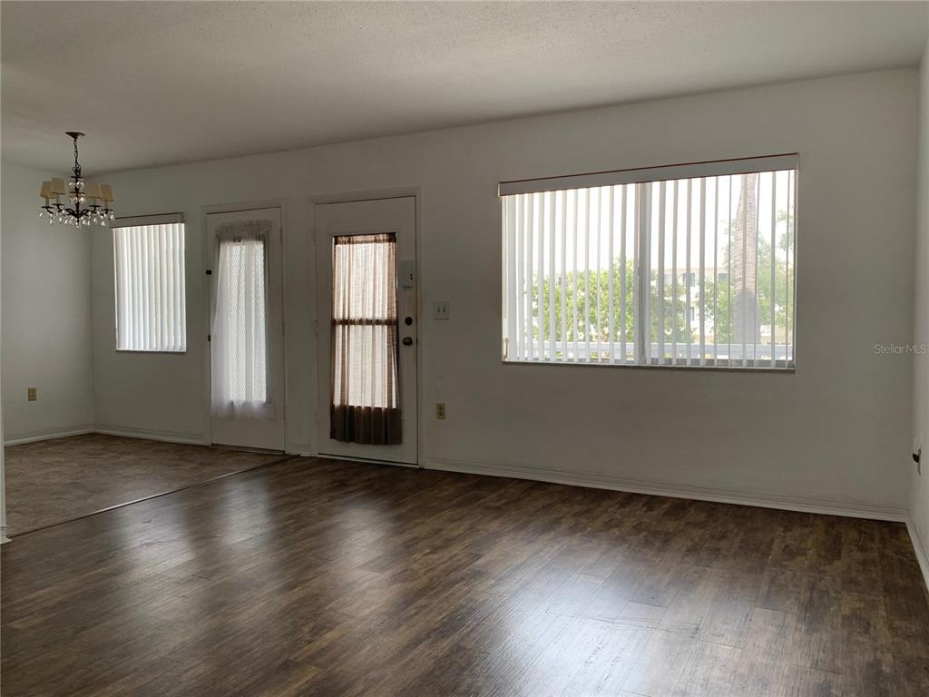 A living room with wood-look flooring, white walls, vertical blinds, and two exterior doors — 8126 112TH STREET UNIT 203, SEMINOLE, FL