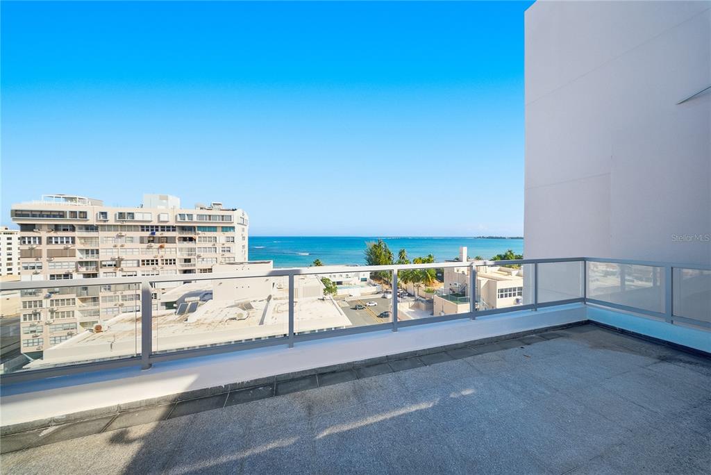 A balcony with a glass railing overlooks a city street and the ocean — 59 LIRIO UNIT 301, CAROLINA, PR