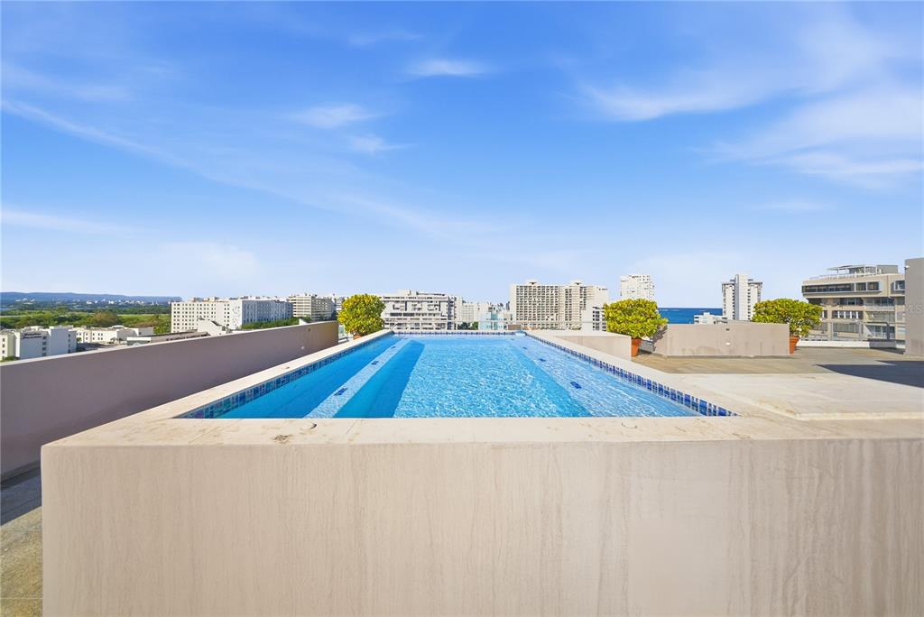 A rooftop infinity pool overlooks a city skyline and the ocean under a blue sky — 59 LIRIO UNIT 301, CAROLINA, PR