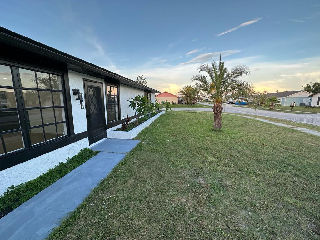 A white stucco house exterior with black trim, a front walkway, and a small palm tree — 13556 ROMFORD AVENUE, PORT CHARLOTTE, FL