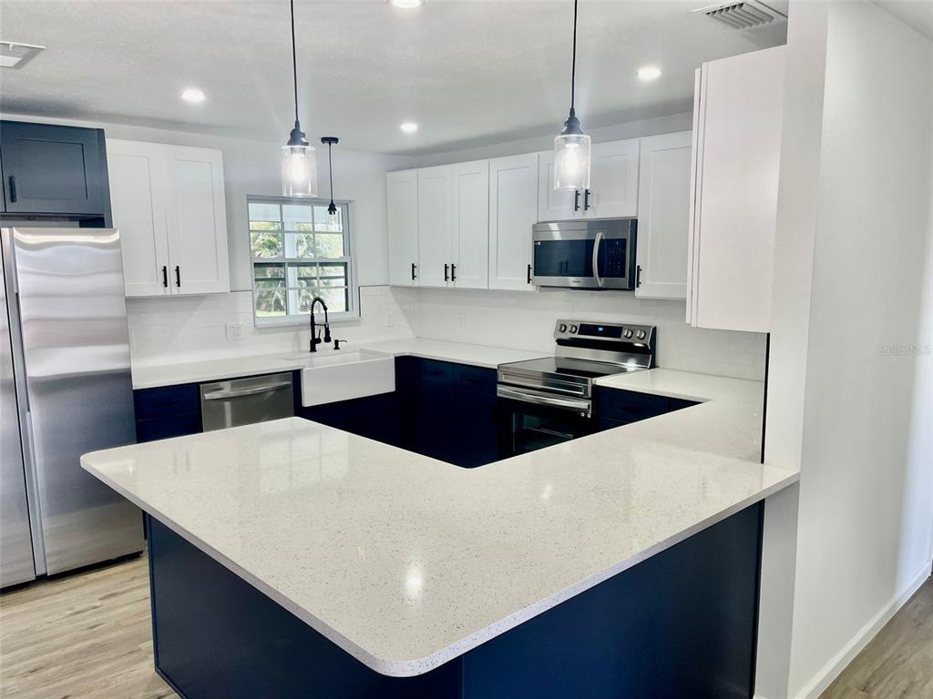A kitchen features white upper cabinets, dark blue lower cabinets, and a white quartz peninsula — 13556 ROMFORD AVENUE, PORT CHARLOTTE, FL