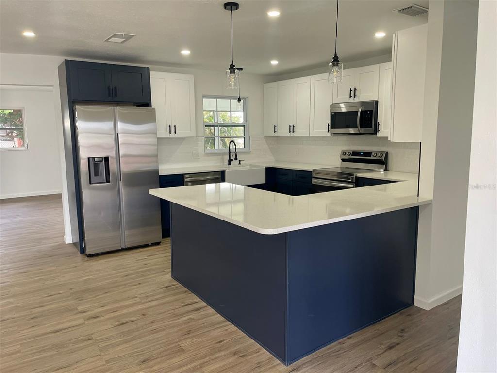 A kitchen with a blue island, white upper cabinets, stainless steel appliances, and light wood flooring — 13556 ROMFORD AVENUE, PORT CHARLOTTE, FL