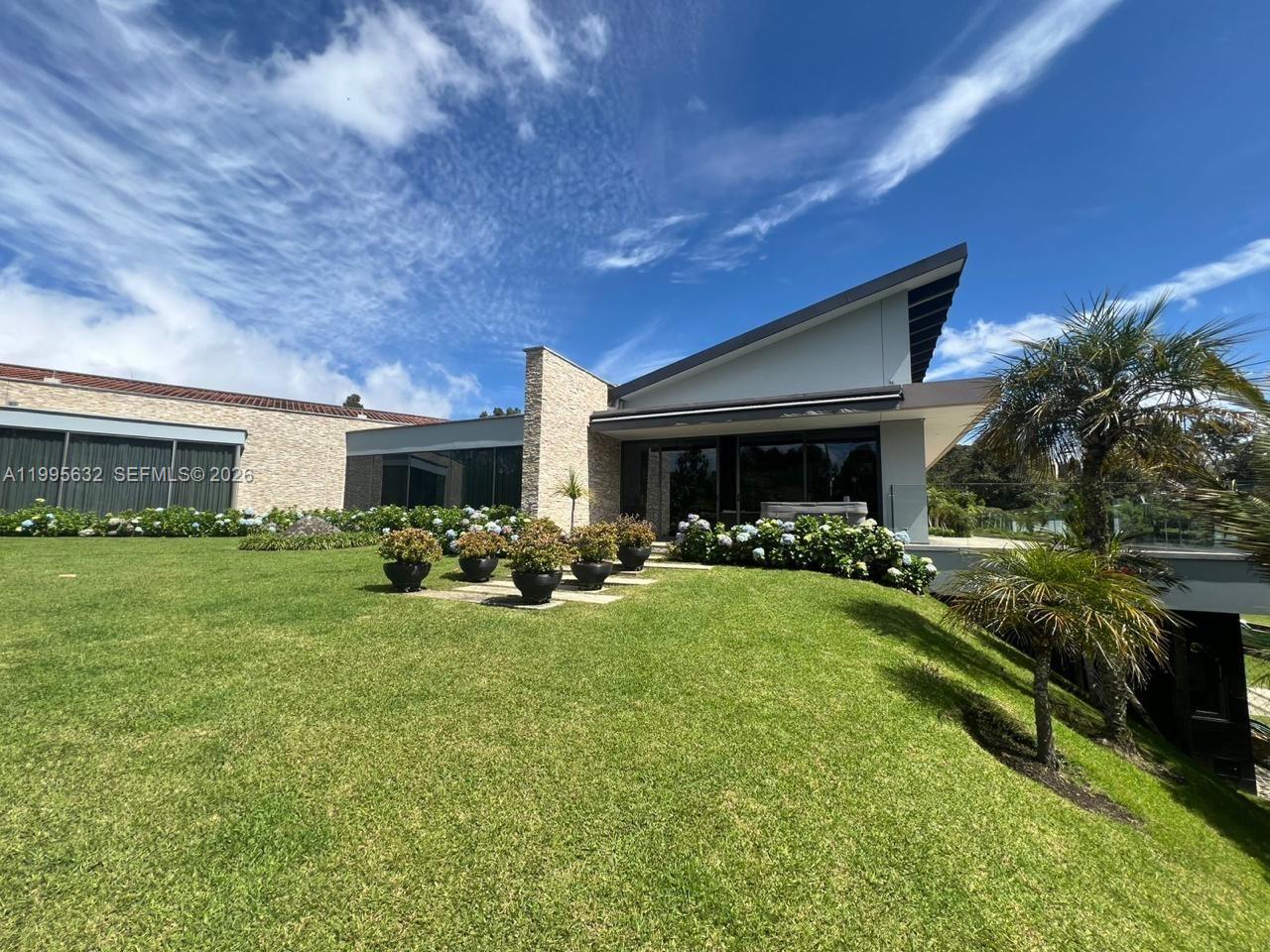 A modern house with a stone accent wall sits above a sloped, grassy lawn — Alto de Las Palmas Km 17, vía La Acuarela, FL