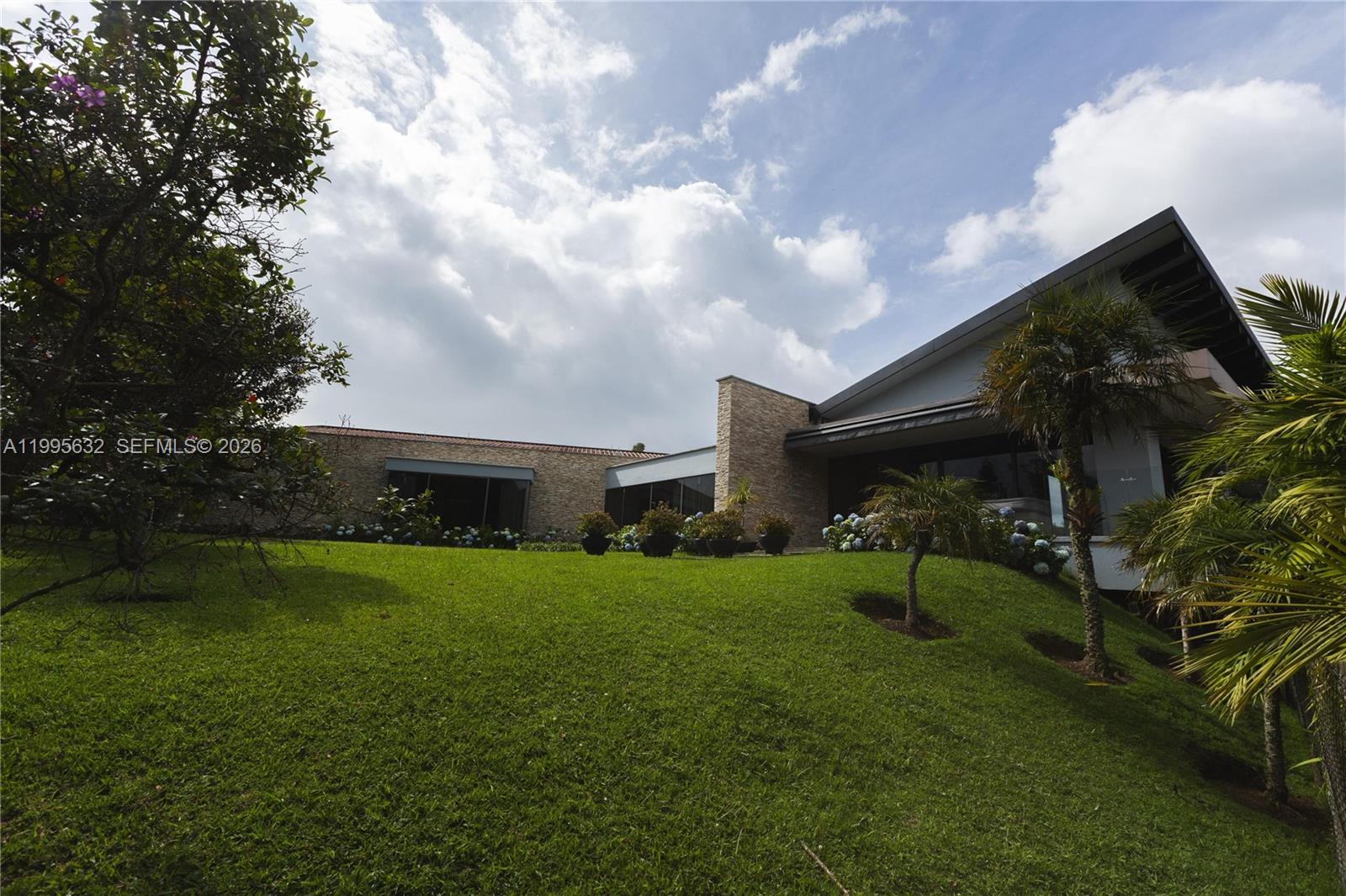 A modern house with stone walls and large windows sits atop a grassy hill — Alto de Las Palmas Km 17, vía La Acuarela, FL