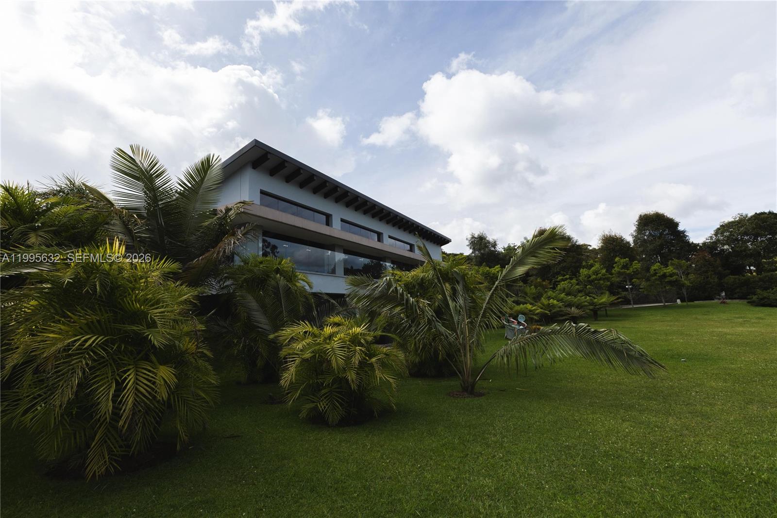 A modern two-story house with large windows sits behind palm trees on a grassy lawn — Alto de Las Palmas Km 17, vía La Acuarela, FL