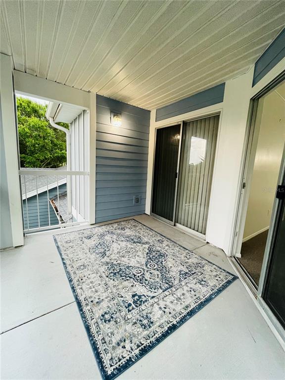 A covered balcony features blue siding, a patterned area rug, and sliding glass doors — 727 SUGAR BAY WAY UNIT 303, LAKE MARY, FL