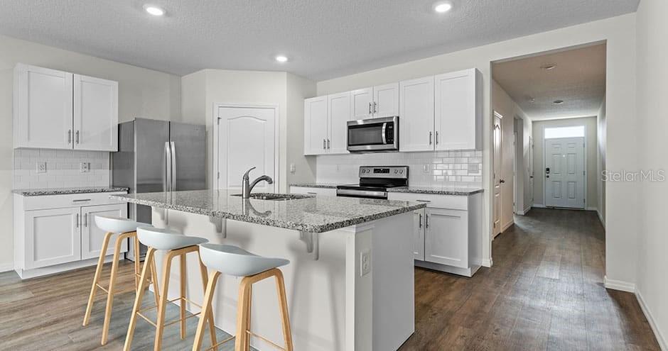 A kitchen features white cabinets, granite countertops, a center island with stools, and stainless appliances — 2429 MAIDENS BLUFF AVENUE UNIT Hayden, DAVENPORT, FL