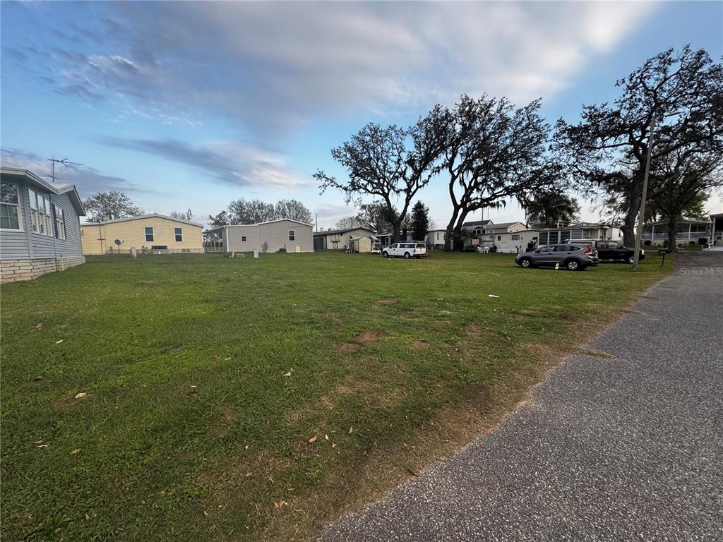 An empty, grassy lot sits between several mobile homes under a partly cloudy sky — 10028 WELLINGTON AVENUE, DADE CITY, FL