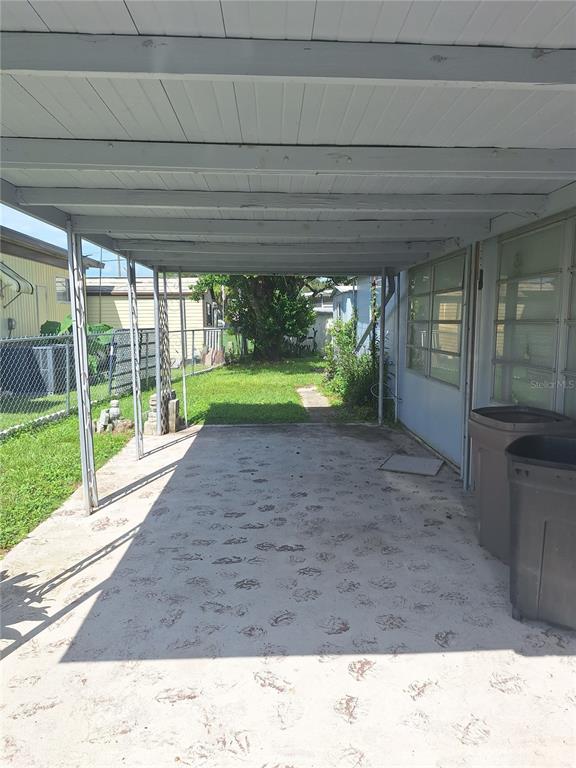 A concrete carport with a white wooden ceiling sits beside a house with two trash cans — 6349 NEW YORK STREET, ZEPHYRHILLS, FL