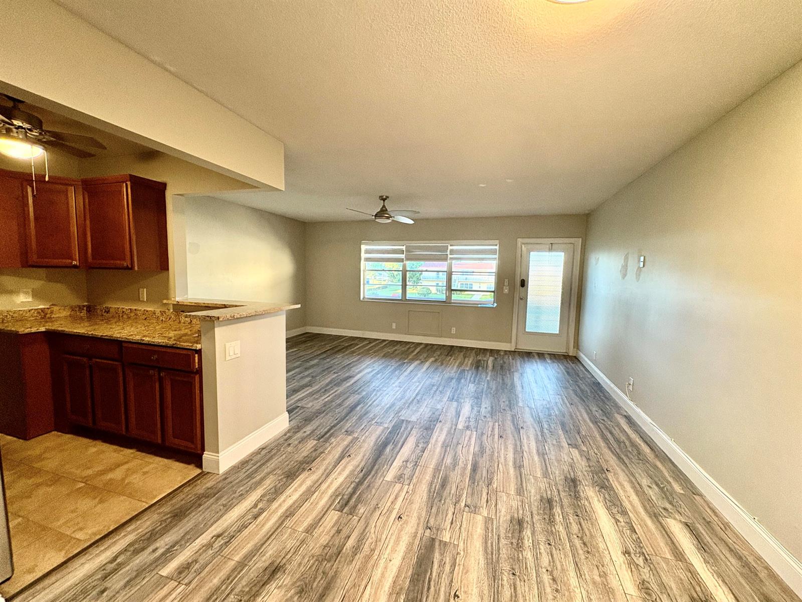 An open-concept living area features wood-look flooring, a kitchen with granite countertops, and a door — 111 E Waltham, West Palm Beach FL 33417, WEST PALM BEACH, FL