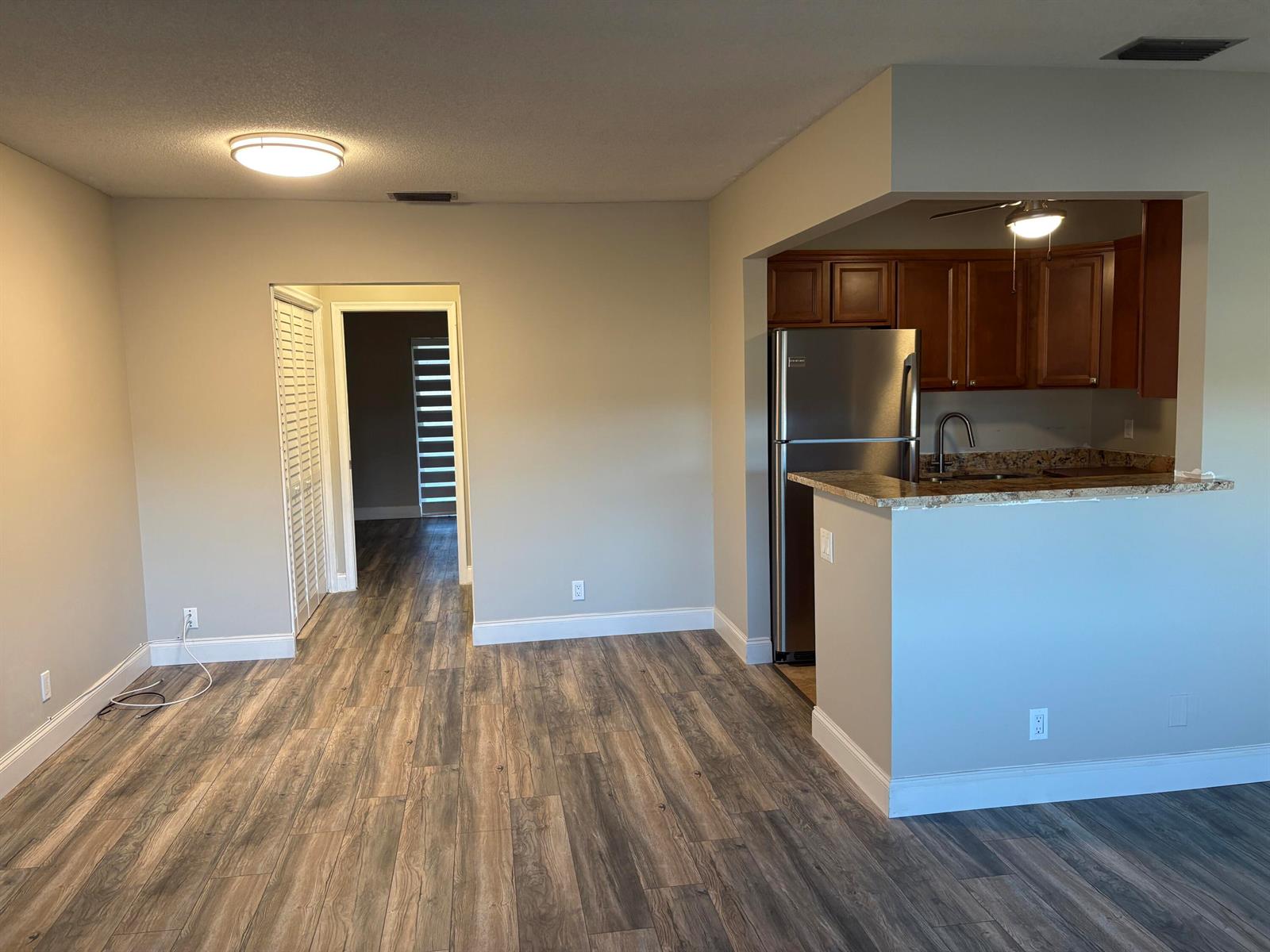A living area with wood-look flooring leads to a kitchen featuring stainless steel appliances — 111 E Waltham, West Palm Beach FL 33417, WEST PALM BEACH, FL