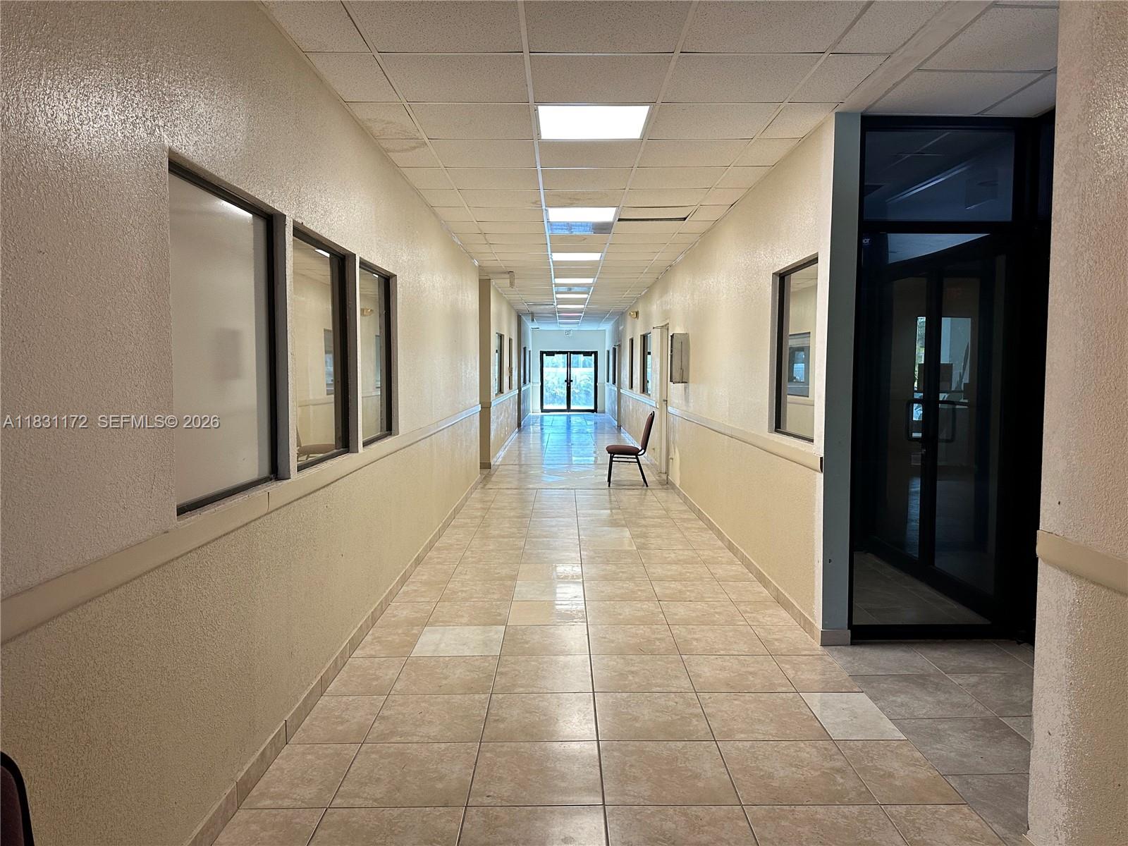 A long, tiled hallway features beige walls, recessed ceiling lights, and a single chair — 2922 N State Road 7 # 2934, Margate FL 33063, MARGATE, FL