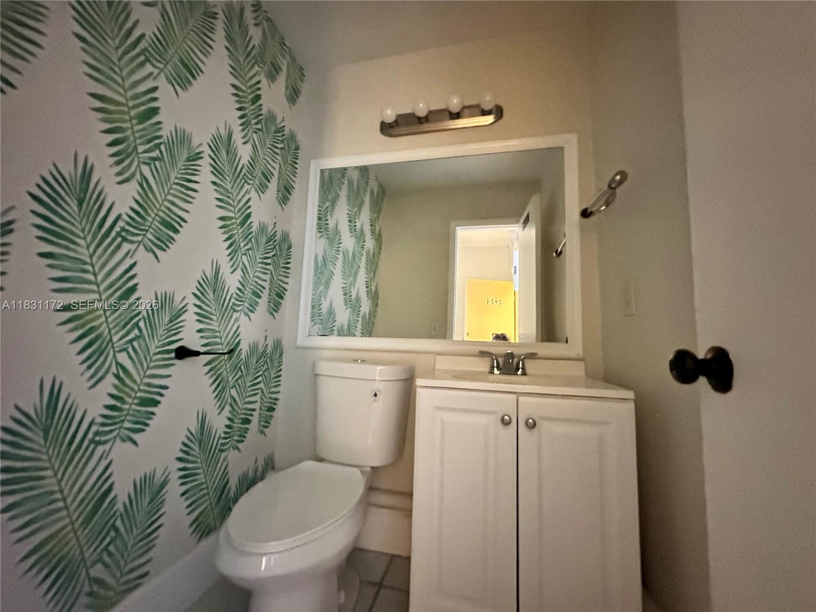 A bathroom features a white vanity, a toilet, and a wall with green palm leaf wallpaper — 2922 N State Road 7 # 2934, Margate FL 33063, MARGATE, FL