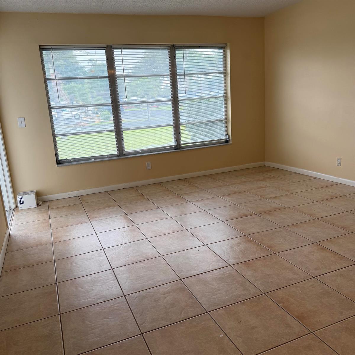An empty room features tan tile flooring, beige walls, and a large three-pane window — 707 High Point Boulevard N Unit C, Delray Beach FL 33445, DELRAY BEACH, FL