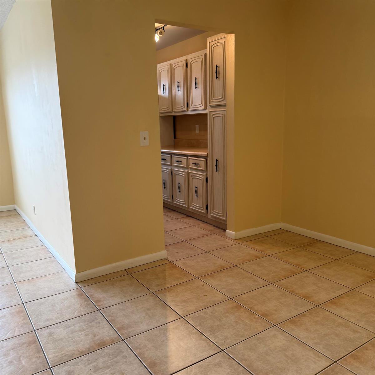 A view from a tiled room looking into a kitchen with light-colored cabinetry — 707 High Point Boulevard N Unit C, Delray Beach FL 33445, DELRAY BEACH, FL