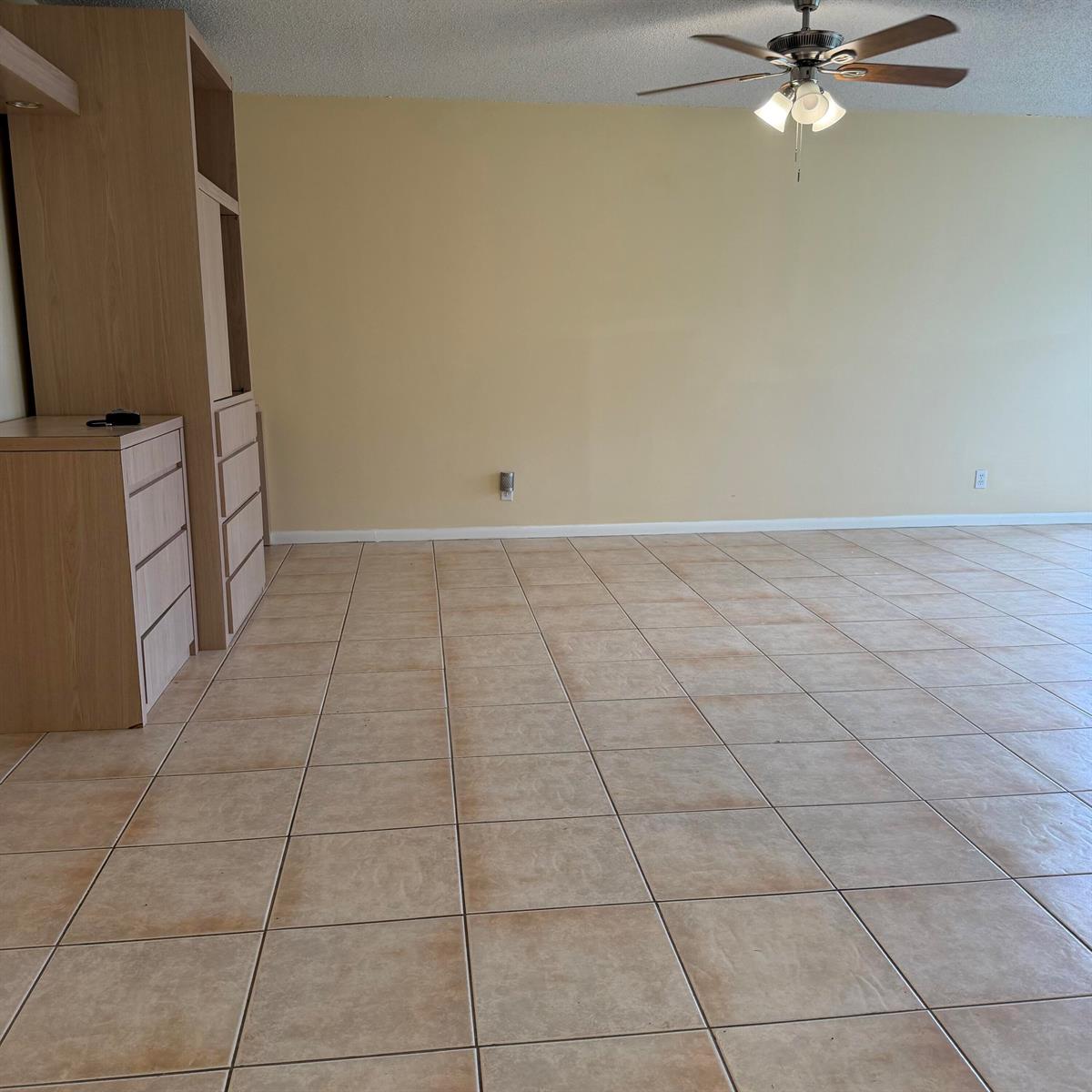 An empty room features light-colored tile flooring, beige walls, and a built-in wooden storage unit — 707 High Point Boulevard N Unit C, Delray Beach FL 33445, DELRAY BEACH, FL