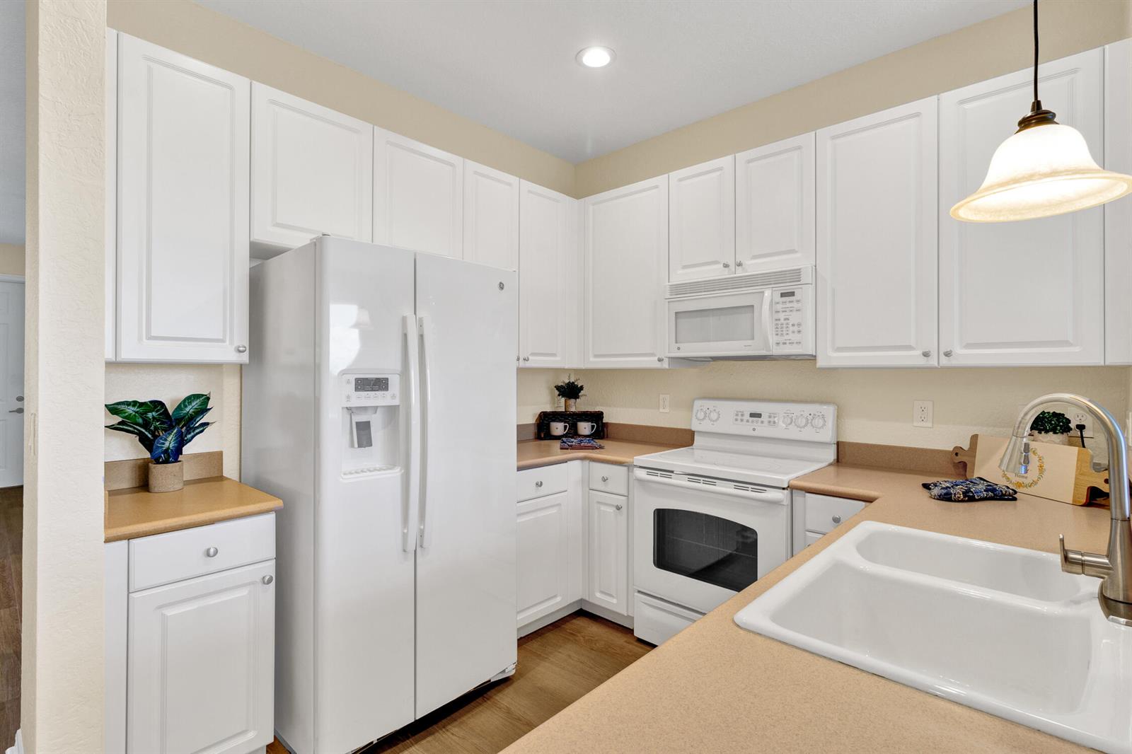 A kitchen with white cabinets, a white refrigerator, a white stove, and tan countertops — 9975 E Villa Circle, Vero Beach FL 32966, VERO BEACH, FL