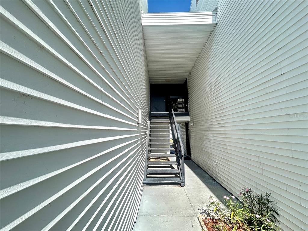 An outdoor staircase leads to a dark entryway between two white vinyl-sided building walls — 705 HAVEN PLACE UNIT 705, TARPON SPRINGS, FL