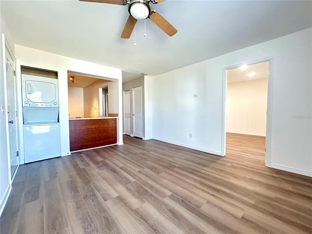A room with wood-look flooring, a ceiling fan, a stacked washer-dryer, and a kitchen pass-through — 705 HAVEN PLACE UNIT 705, TARPON SPRINGS, FL