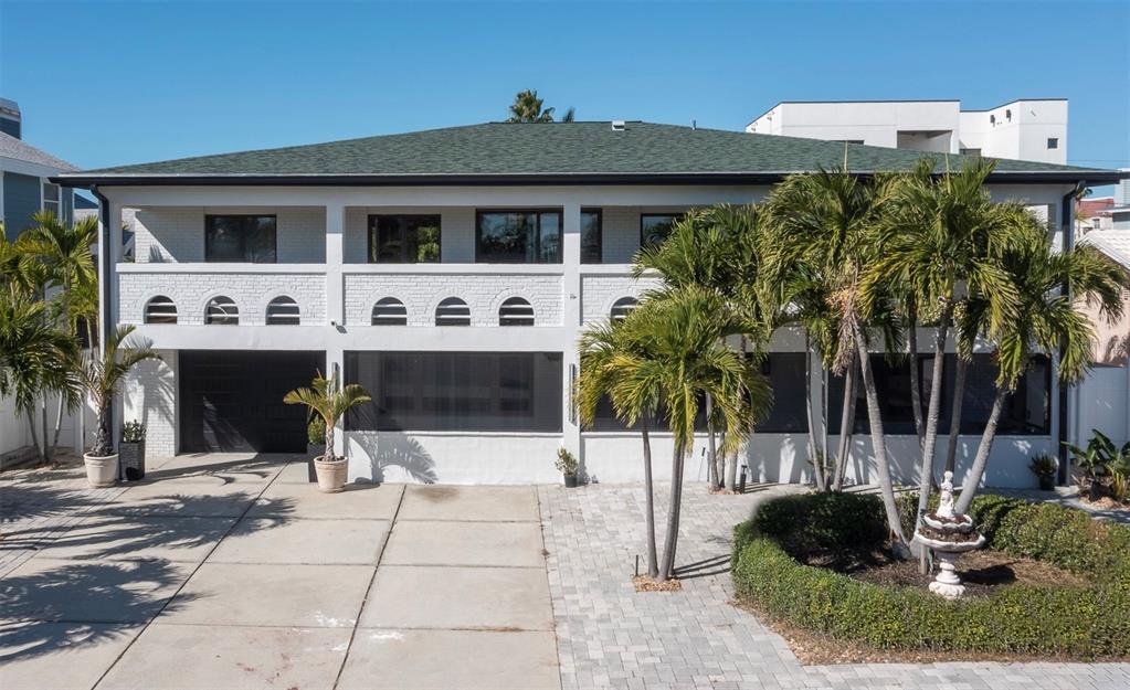 A two-story white brick house with a green roof, palm trees, and a paved driveway — 2710 HIBISCUS DRIVE W, BELLEAIR BEACH, FL