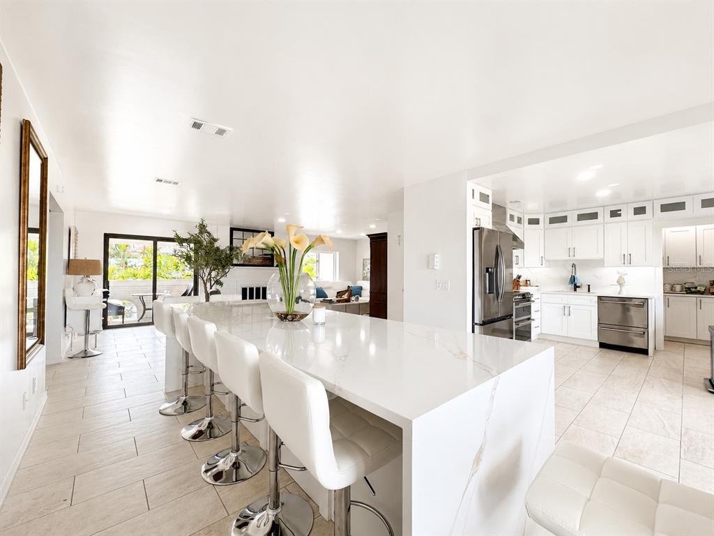 A modern kitchen features a large white quartz waterfall island with bar stools and stainless appliances — 2710 HIBISCUS DRIVE W, BELLEAIR BEACH, FL