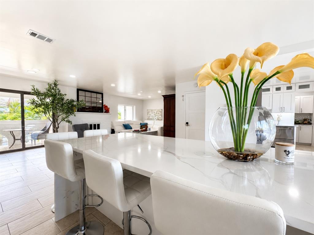 A kitchen island with white marble countertops and bar stools overlooks a living room area — 2710 HIBISCUS DRIVE W, BELLEAIR BEACH, FL