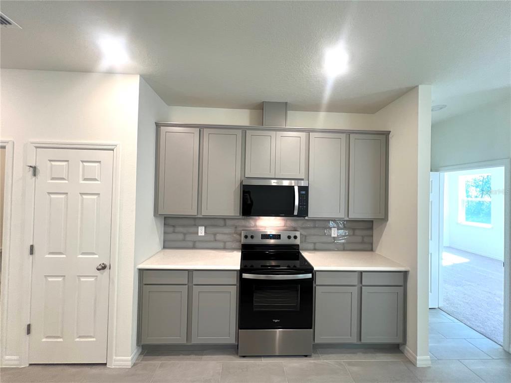 A kitchen features gray cabinets, stainless steel appliances, a white countertop, and a tiled backsplash — 4 LYNBROOK DRIVE, PALM COAST, FL
