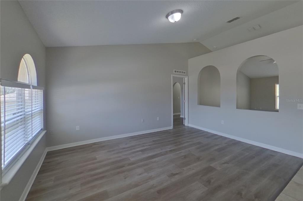 An empty room features light gray walls, wood-look flooring, arched wall niches, and a window — 921 JAYHIL DRIVE, MINNEOLA, FL