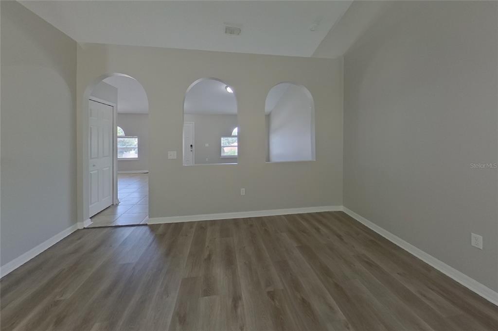 An empty room features light gray walls, wood-look flooring, and three arched wall openings — 921 JAYHIL DRIVE, MINNEOLA, FL