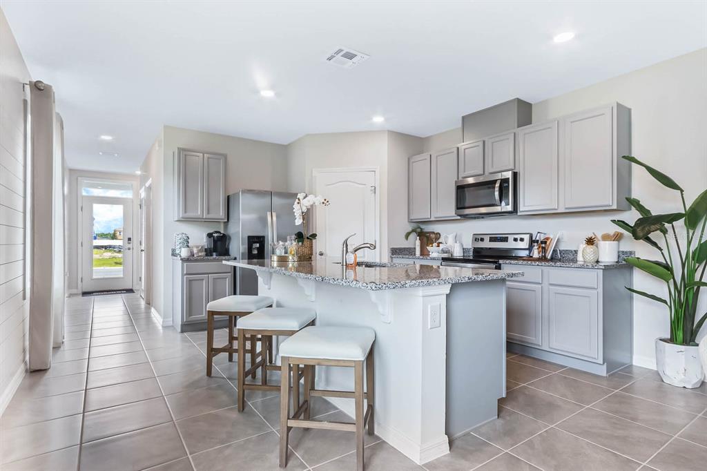 A kitchen features gray cabinets, granite countertops, a central island with bar stools, and tile flooring — 3459 SABATIA LANE, POINCIANA, FL