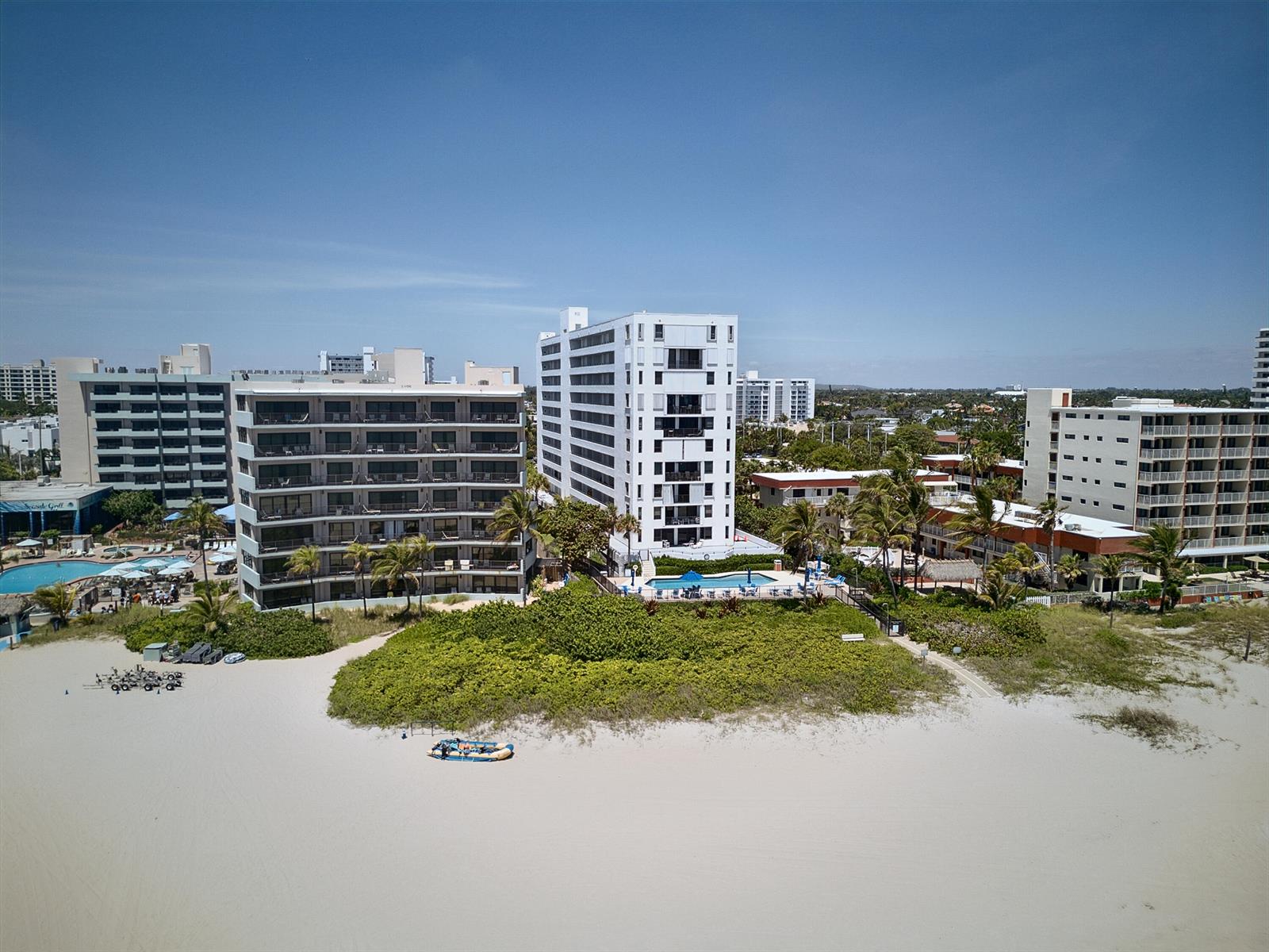 An aerial view of beachfront apartment buildings with swimming pools and surrounding tropical landscaping — 1500 N Ocean Boulevard # 803, Pompano Beach FL 33062, POMPANO BEACH, FL