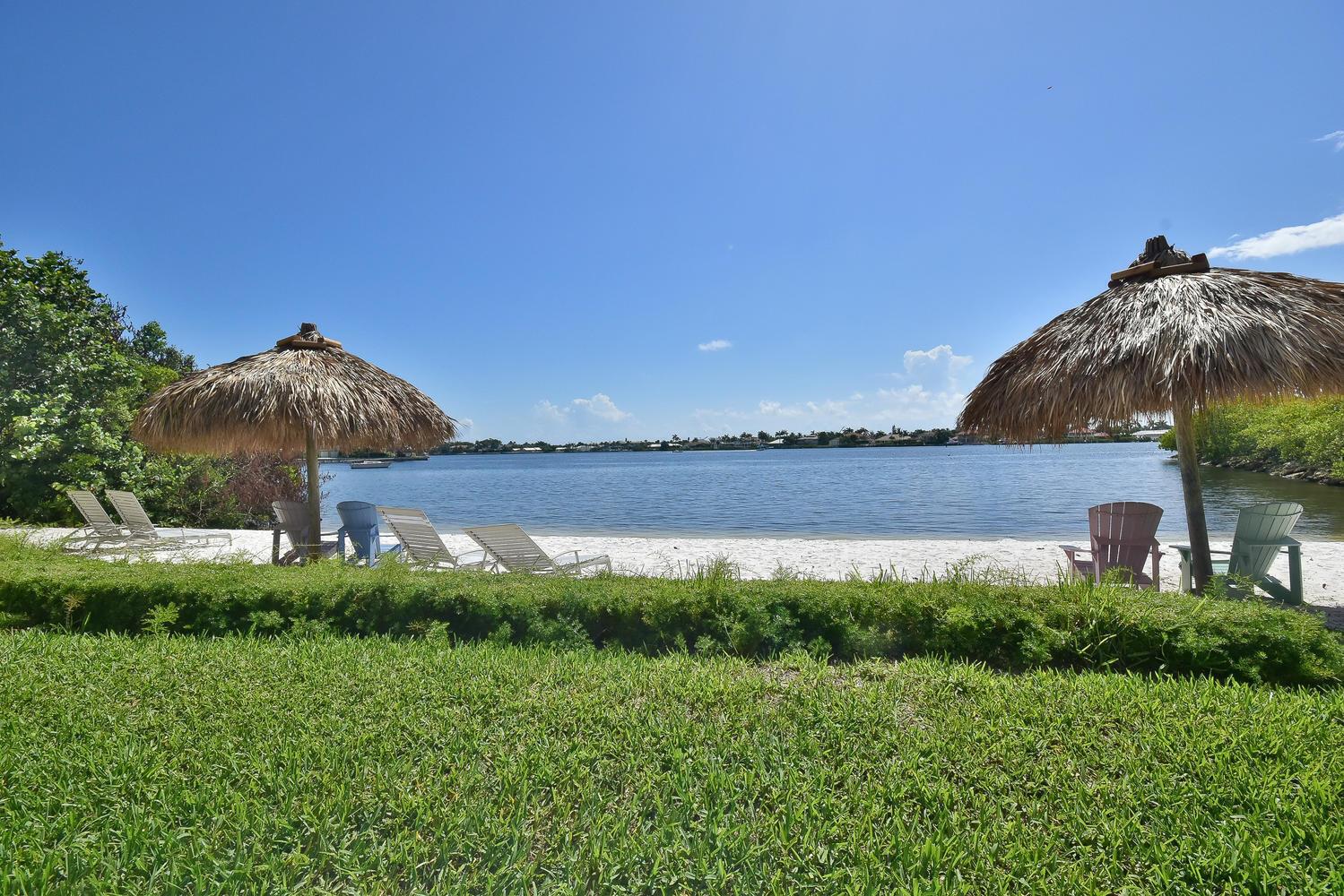 A sandy beach with thatched umbrellas and chairs overlooks a calm bay under blue skies — 1200 Scotia Drive # 403, Hypoluxo FL 33462, HYPOLUXO, FL