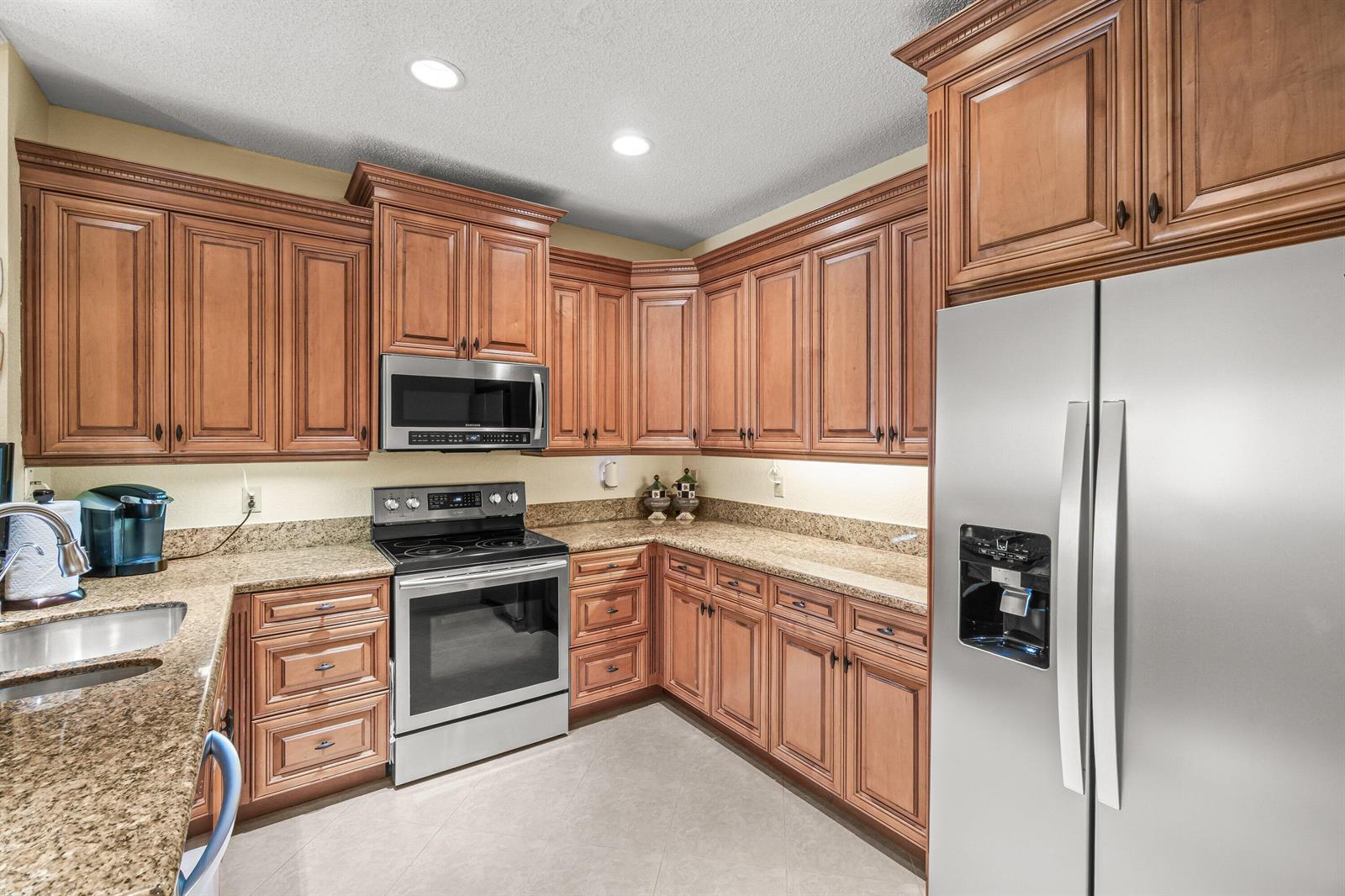 A kitchen features wood cabinets, granite countertops, stainless steel appliances, and tile flooring — 6229 Graycliff Drive # D, Boca Raton FL 33496, BOCA RATON, FL