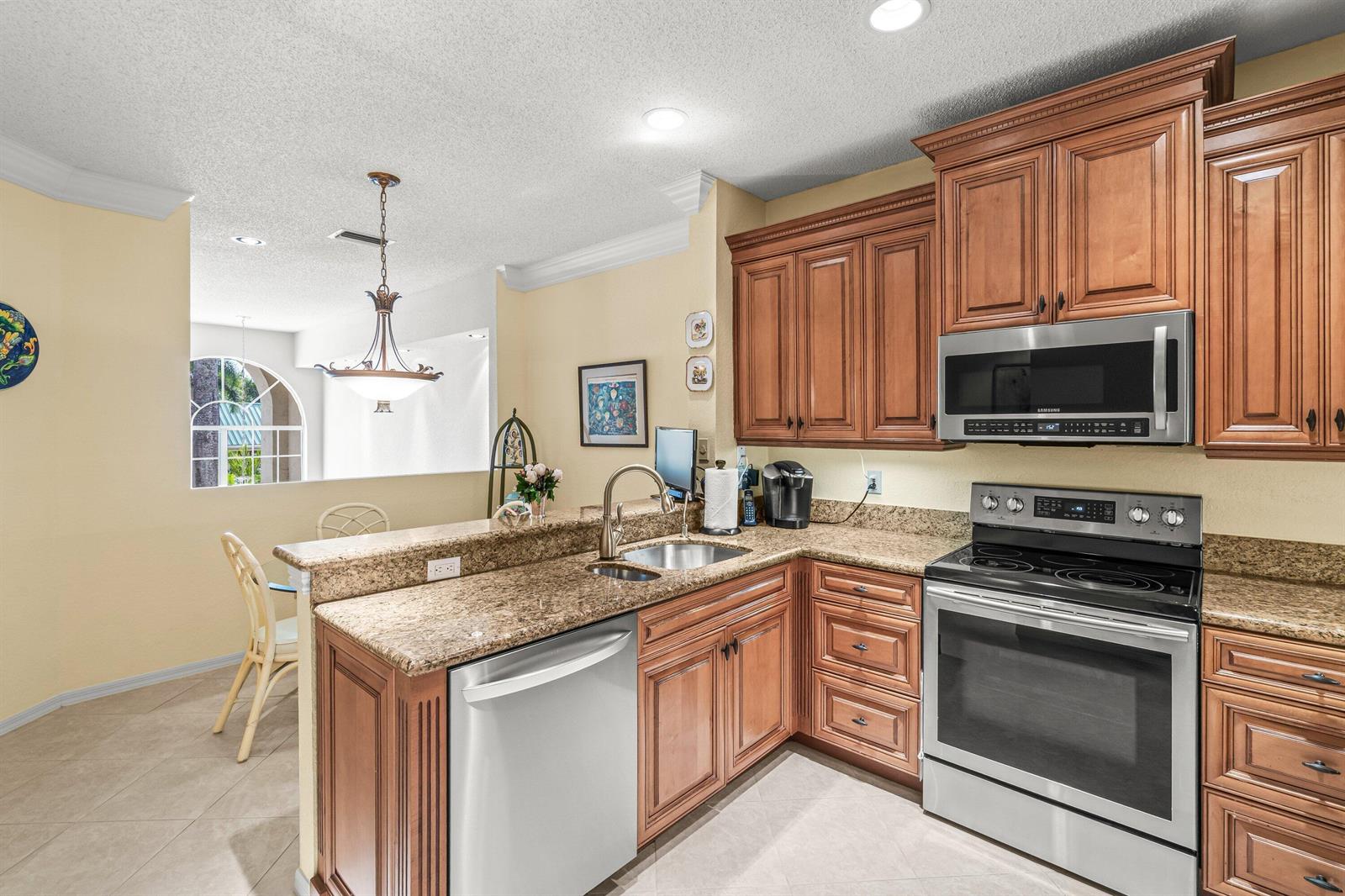 A kitchen features wood cabinets, granite countertops, stainless steel appliances, and a breakfast bar area — 6229 Graycliff Drive # D, Boca Raton FL 33496, BOCA RATON, FL