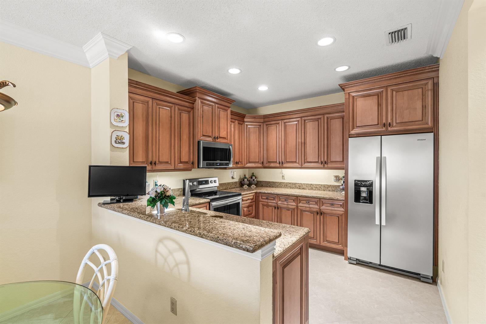 A kitchen features wood cabinets, granite countertops, stainless steel appliances, and a breakfast bar — 6229 Graycliff Drive # D, Boca Raton FL 33496, BOCA RATON, FL