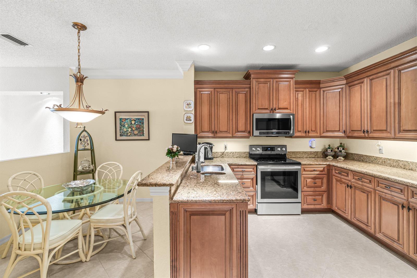 A kitchen with wood cabinets, granite countertops, and an adjacent glass-topped dining table — 6229 Graycliff Drive # D, Boca Raton FL 33496, BOCA RATON, FL