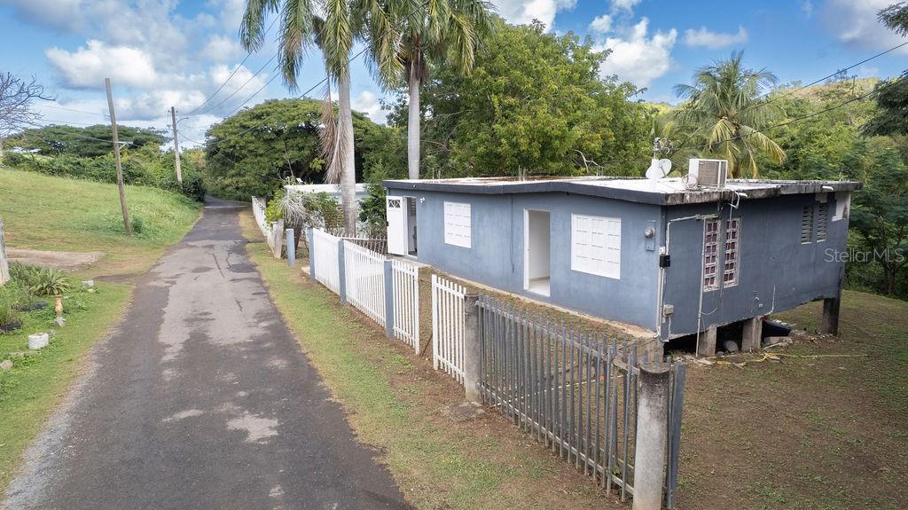 A gray, elevated house sits beside a paved road with a white metal fence — 63 SECTOR VILLA BORINQUEN, VIEQUES, PR