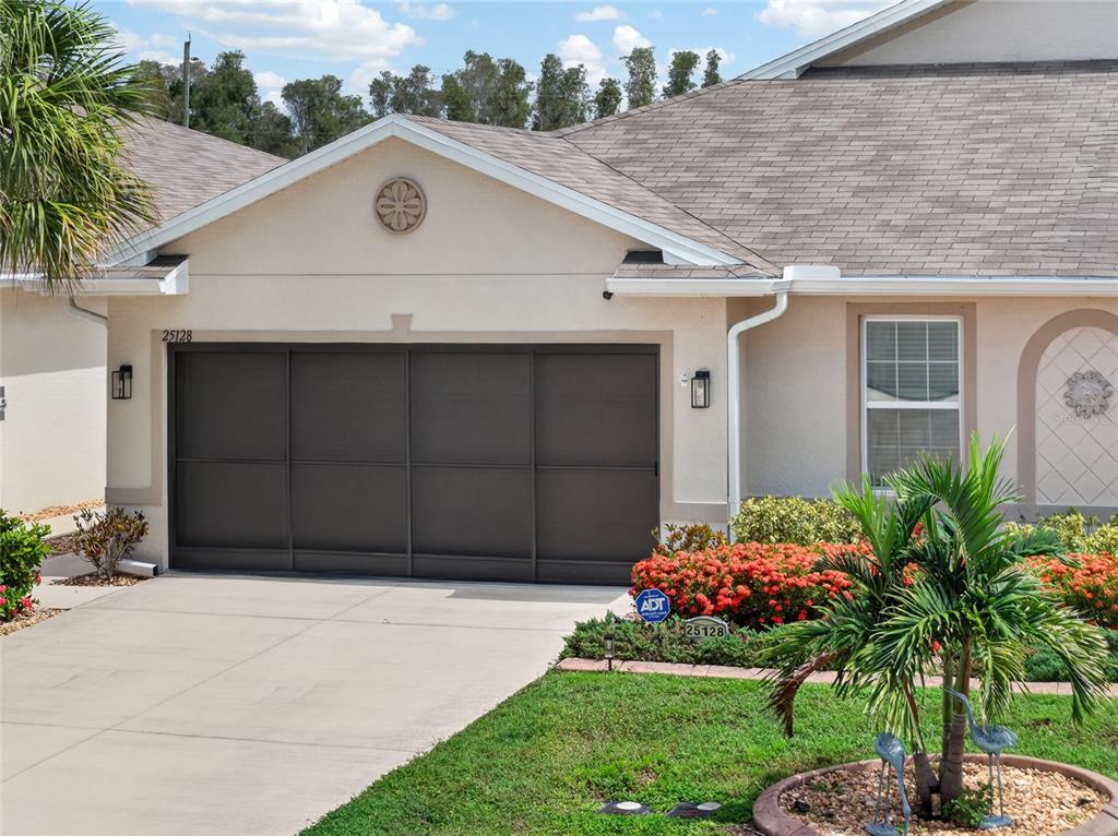 A beige house exterior features a dark garage door, a shingled roof, and landscaping — 25128 E LENOX CIRCLE, PUNTA GORDA, FL