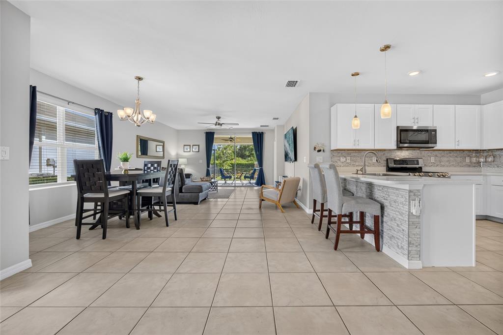 An open-concept kitchen, dining area, and living room feature tile flooring and white cabinetry — 25128 E LENOX CIRCLE, PUNTA GORDA, FL